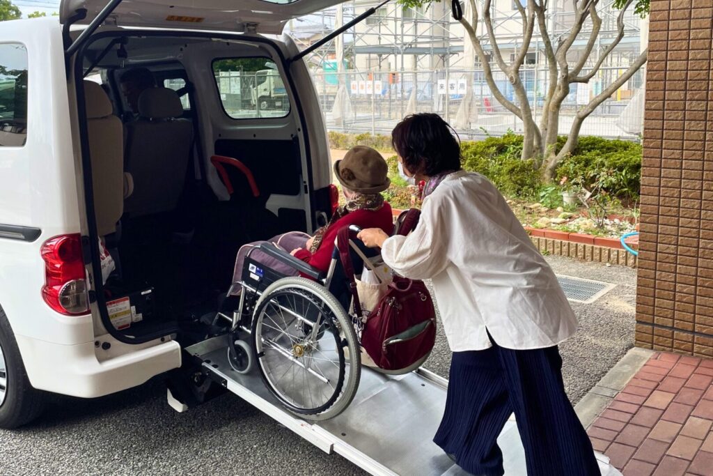 車椅子に乗った高齢者を車に乗せるに介護スタッフ